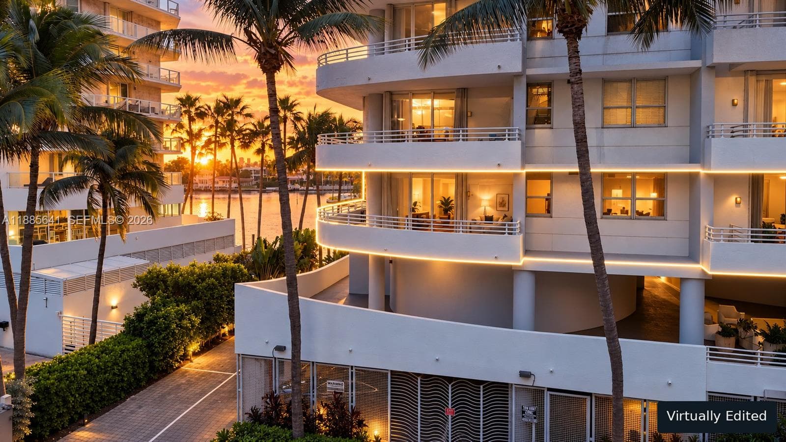 Waterfront mid-rise structure featuring curved balconies with integrated lighting, paved exterior pathways, and mature palm landscaping