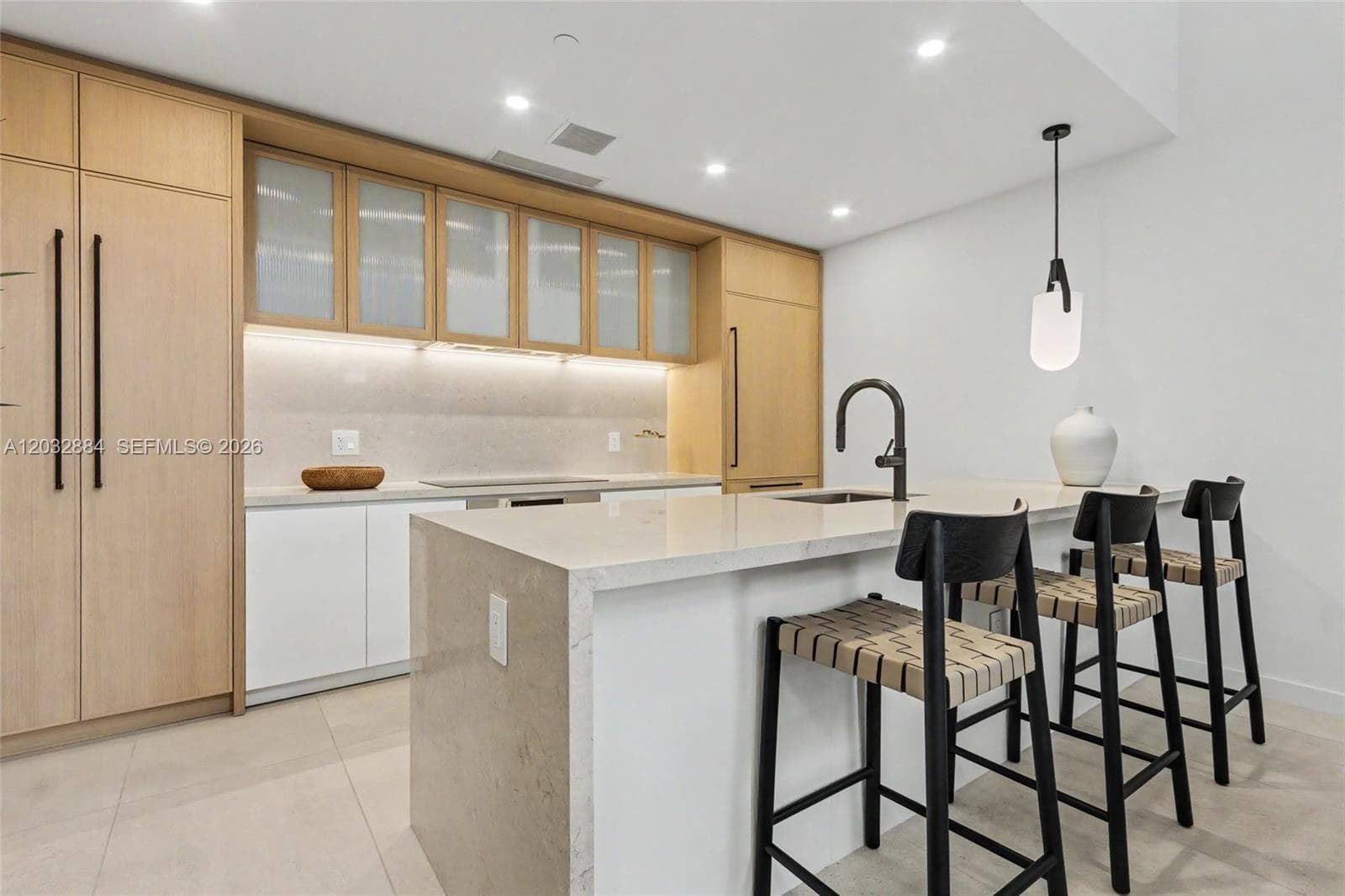 Custom light-wood cabinetry with integrated panel-ready appliances, quartz countertops, central kitchen island with waterfall edge, matte black hardware, and recessed ceiling lighting