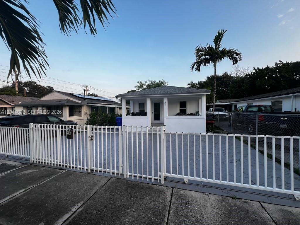 Exterior facade featuring a covered front porch, white exterior finish, gray shingle roof, paved driveway, and metal perimeter fencing