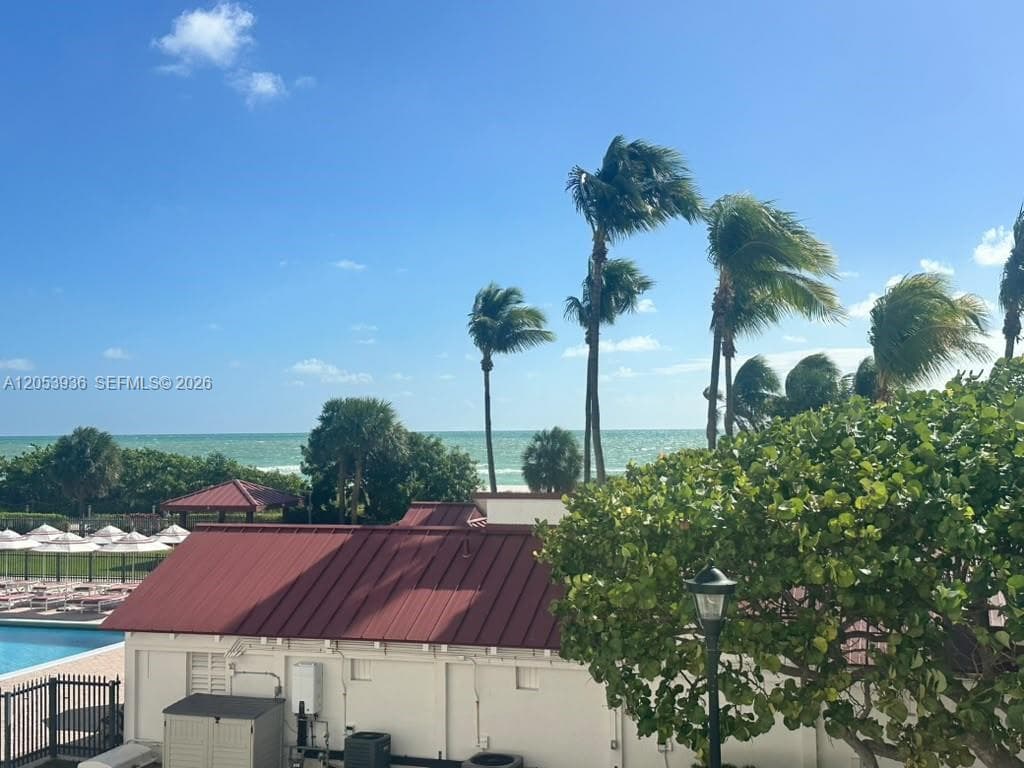 Coastal property featuring a metal roof, swimming pool with deck, and mature palm trees with an ocean backdrop