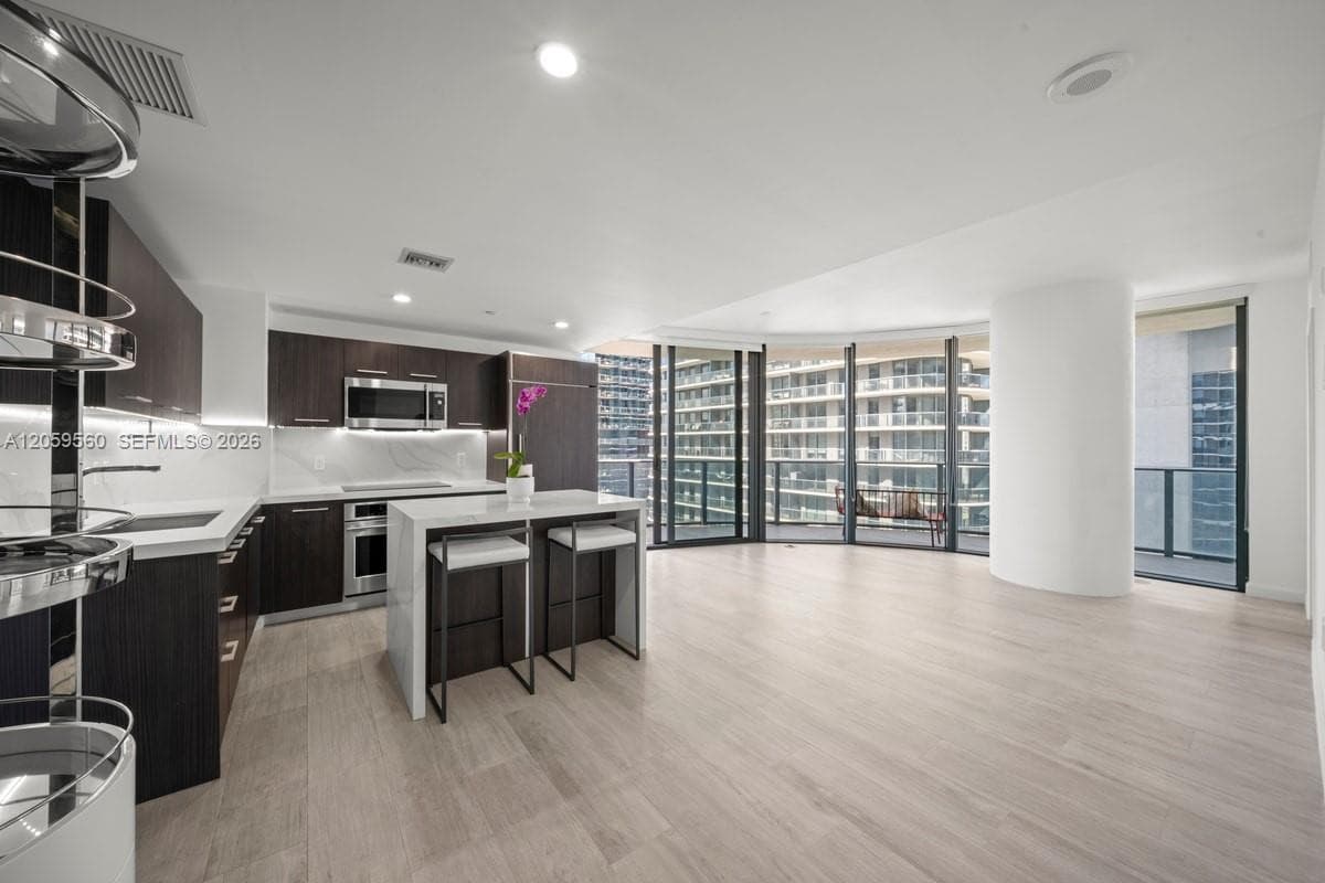Kitchen featuring dark wood-finish cabinetry, quartz countertops, integrated stainless steel appliances, and wood-finish flooring, complemented by floor-to-ceiling windows