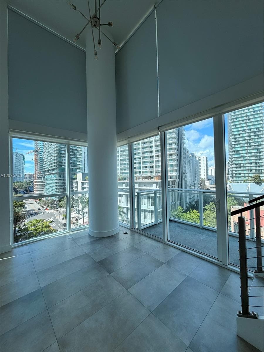 Double-height ceilings, floor-to-ceiling windows, large-format tile flooring, industrial-style structural column, and a balcony with metal railing