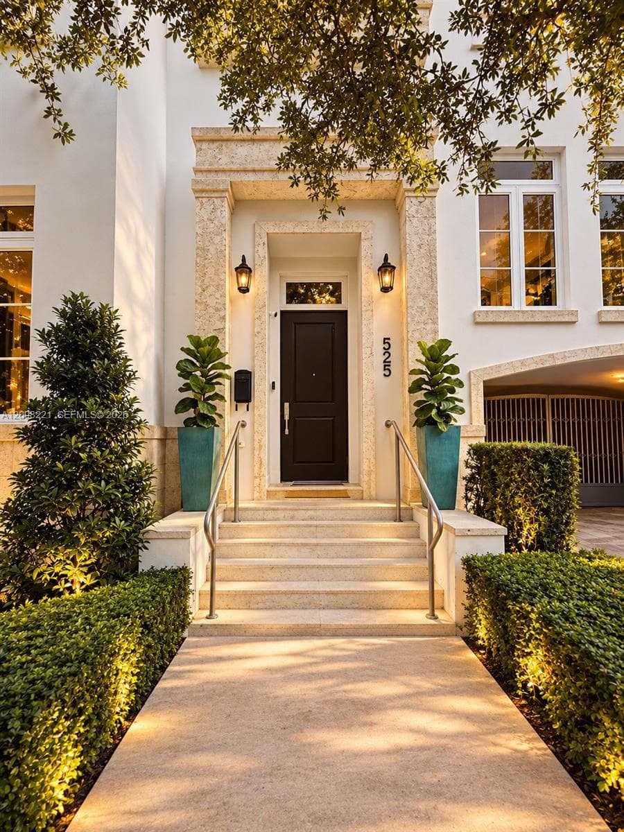 Stucco facade featuring a textured stone door surround, elevated concrete entry steps with metal railings, and dual exterior wall-mounted lanterns