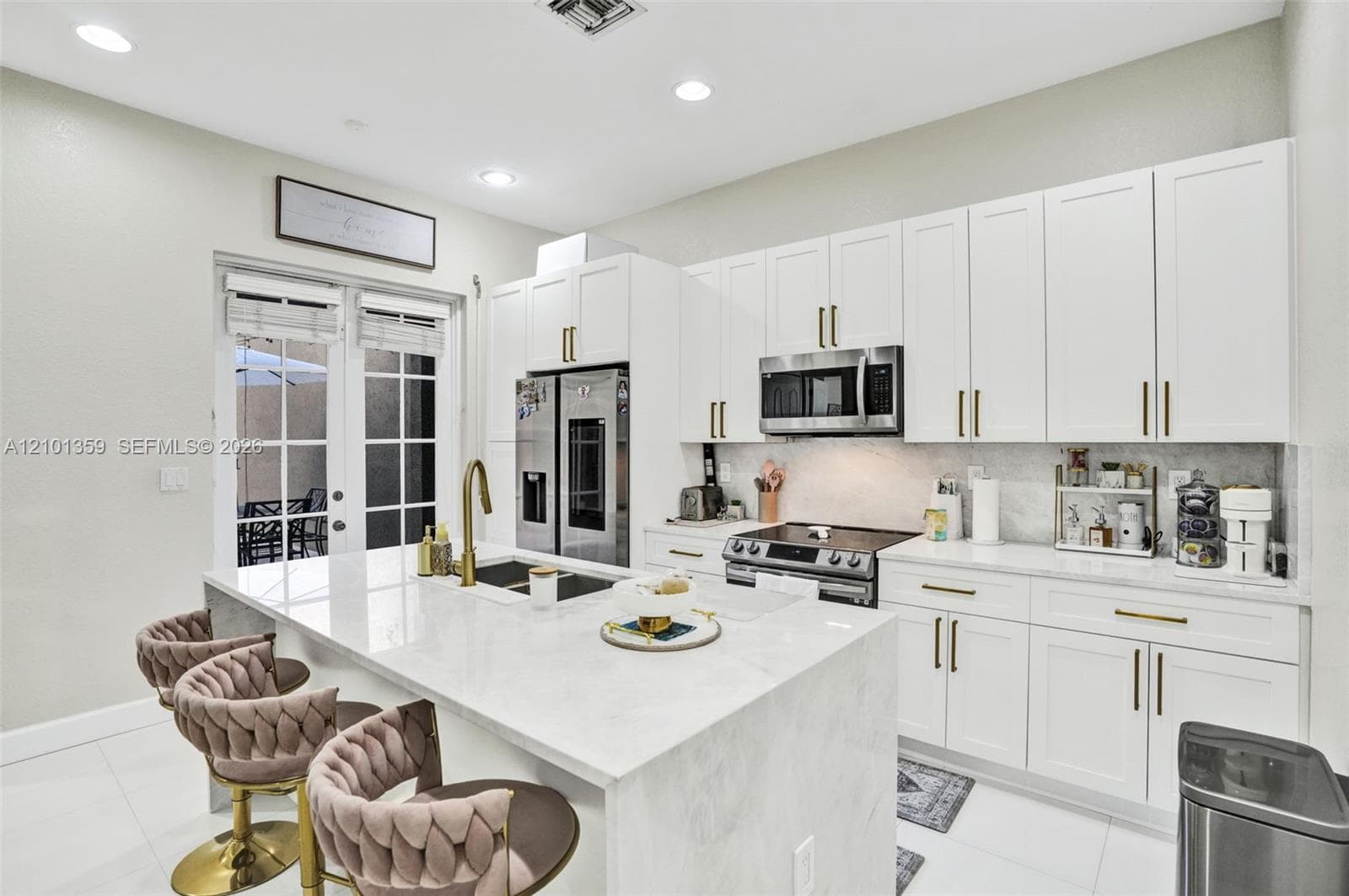 Kitchen featuring white shaker-style cabinetry, quartz countertops with a waterfall-edge island, stainless steel appliances, and gold-finish hardware