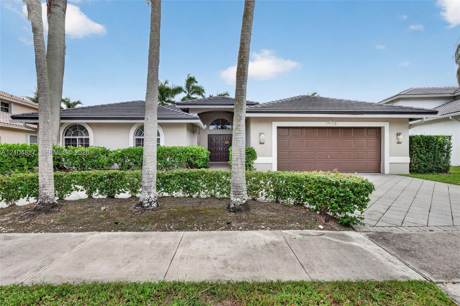 Single-story residence featuring a tile roof, arched windows, dual-entry wood doors, and a paved driveway