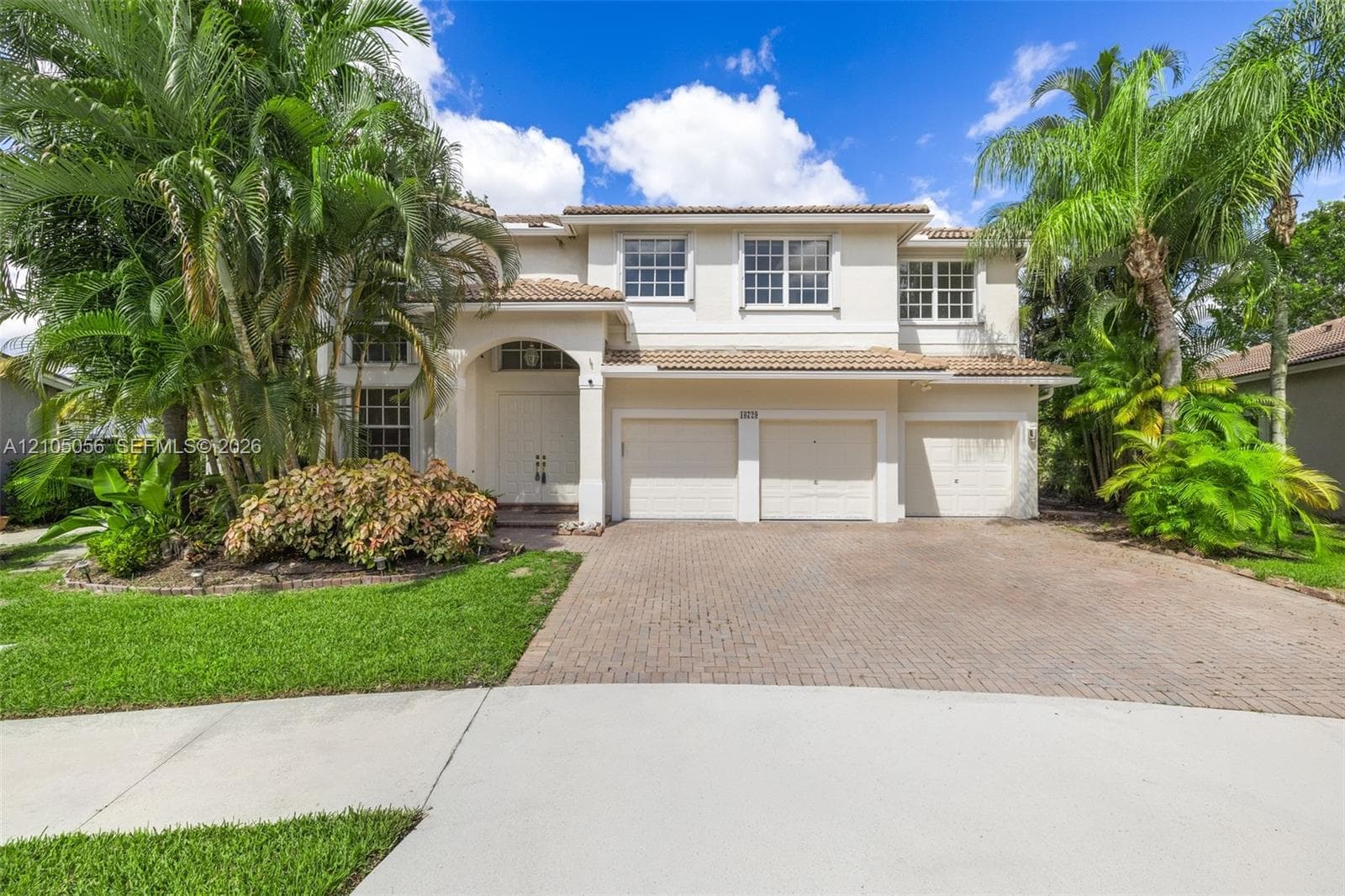 Two-story residence featuring a tile roof, stucco exterior, three-car garage, and paver driveway