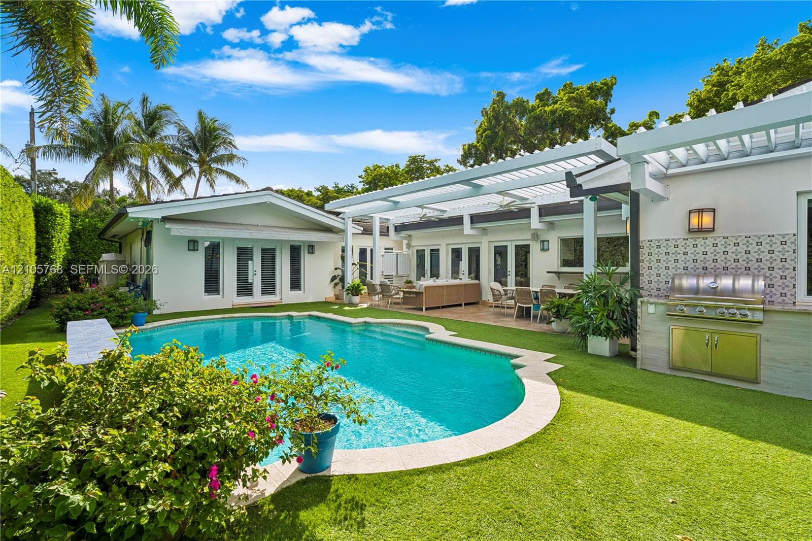 Outdoor patio featuring a white louvered pergola, an in-ground swimming pool with stone coping, a built-in stainless steel outdoor kitchen, and manicured turf