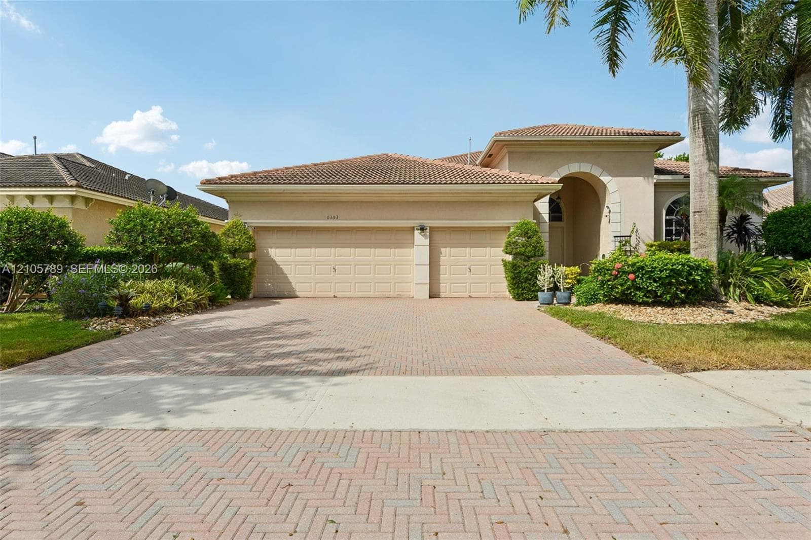 Stucco exterior with a tiled roof, arched entryway, two-car garage, and herringbone-patterned paved driveway
