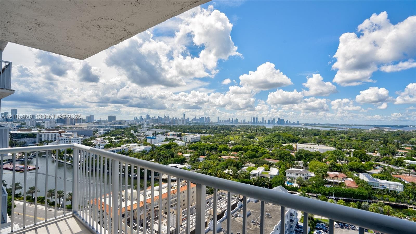 Private balcony with metal railings overlooking an expansive cityscape, waterway, and dense tree canopy