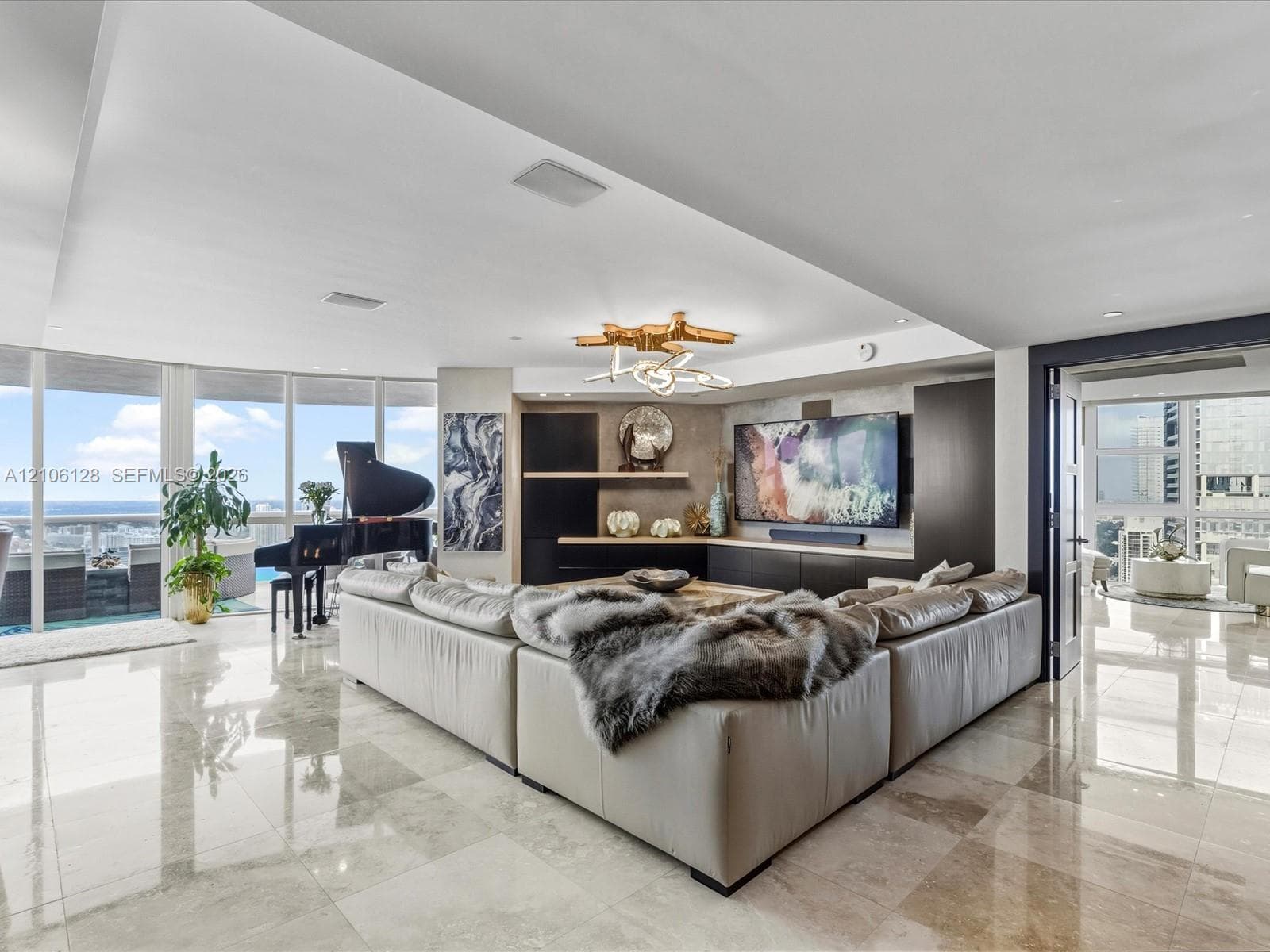 Open-concept interior featuring floor-to-ceiling windows, polished stone flooring, custom dark wood built-in cabinetry, and a tiered modern chandelier