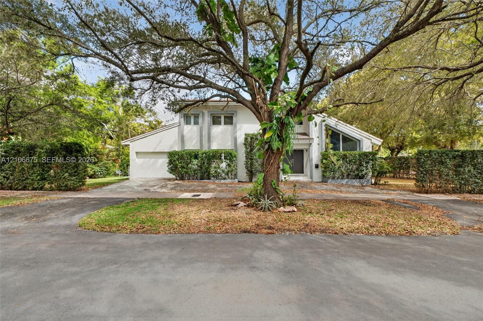 Stucco exterior residence featuring an attached garage, geometric window placements, an asphalt driveway, and mature canopy trees