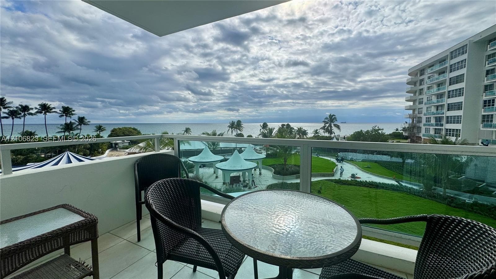 Covered balcony featuring glass paneled railings, white tile flooring, and direct oceanfront scenery