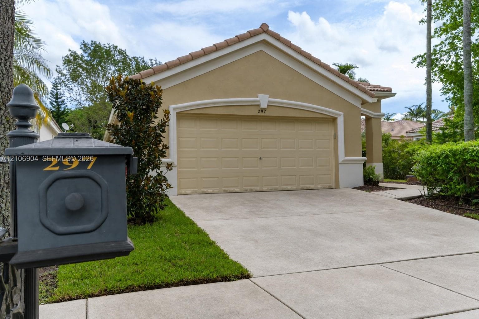 Exterior featuring a neutral-toned stucco facade, a tile roof, an arched garage door, a paved driveway, and a custom metal mailbox