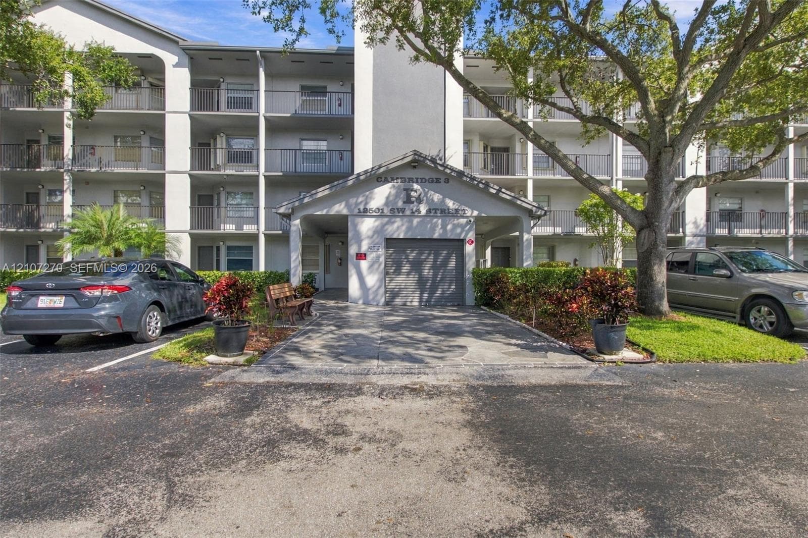 Multi-story exterior featuring a covered entryway, private garage, tiered balconies with metal railings, and mature landscaping