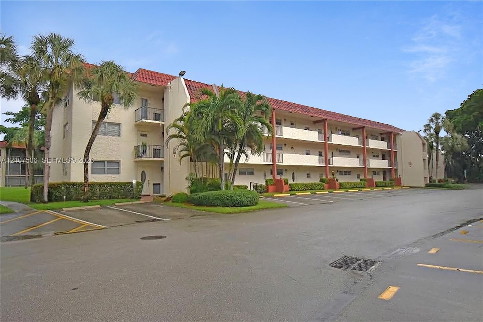 Multi-level exterior featuring a stucco facade, red tile roofing, private balcony spaces, and mature palm trees