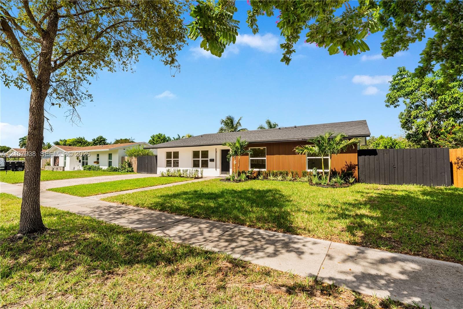 Single-story residence featuring a mid-century modern aesthetic, wood-panel siding, white stucco exterior, asphalt shingle roof, and a black privacy fence