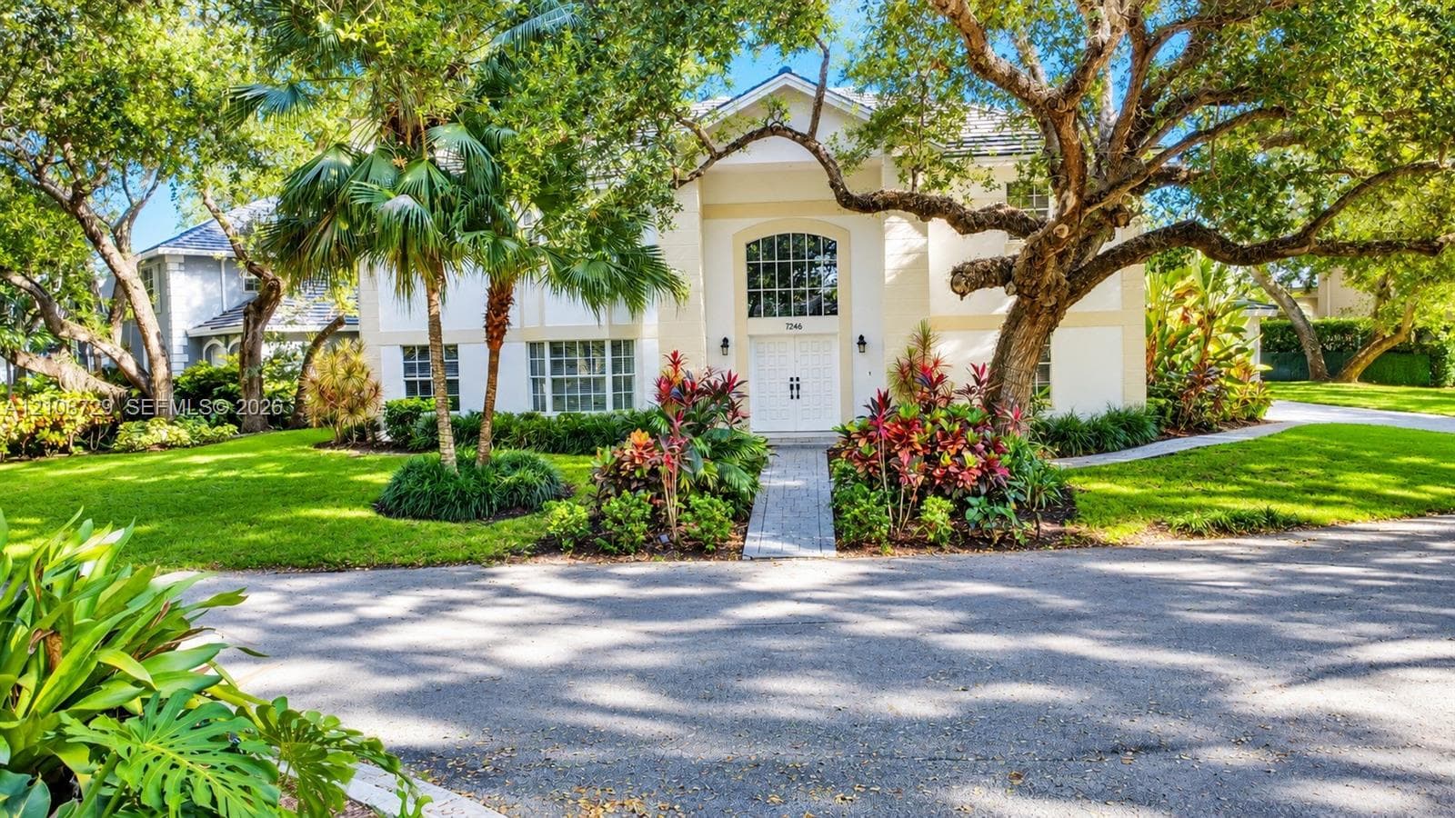 Two-story exterior featuring a high-pitched roofline, an arched transom window above double entry doors, a stone-paver walkway, and mature landscaping