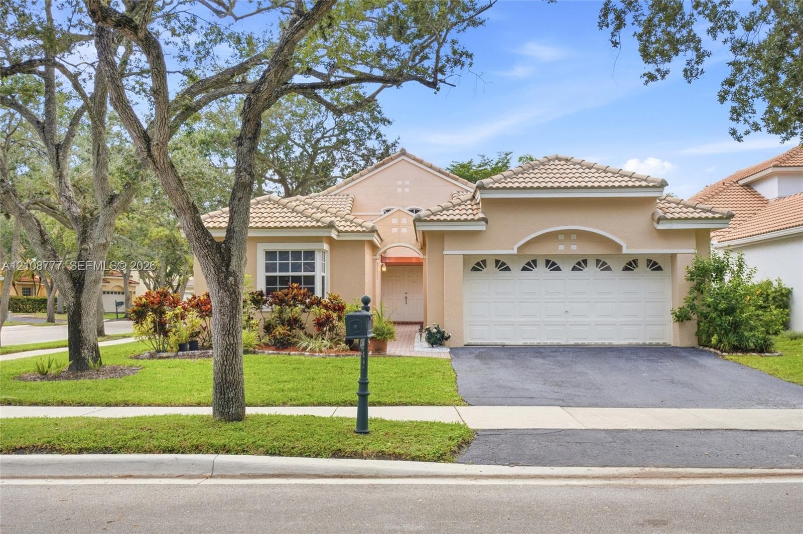 Stucco exterior featuring a tile roof, arched entryway detail, double-car garage, and mature landscape