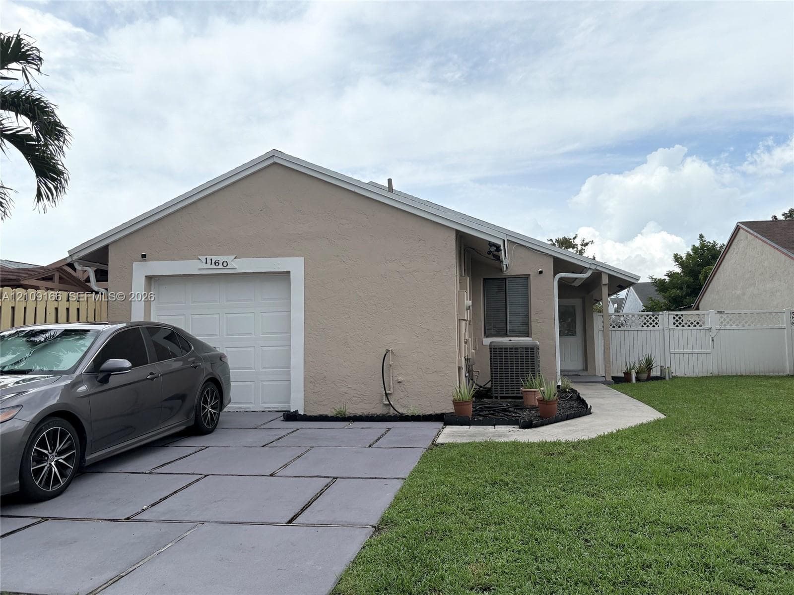 Single-story exterior featuring a textured stucco finish, concrete slab driveway, one-car garage, and perimeter lattice-topped privacy fencing