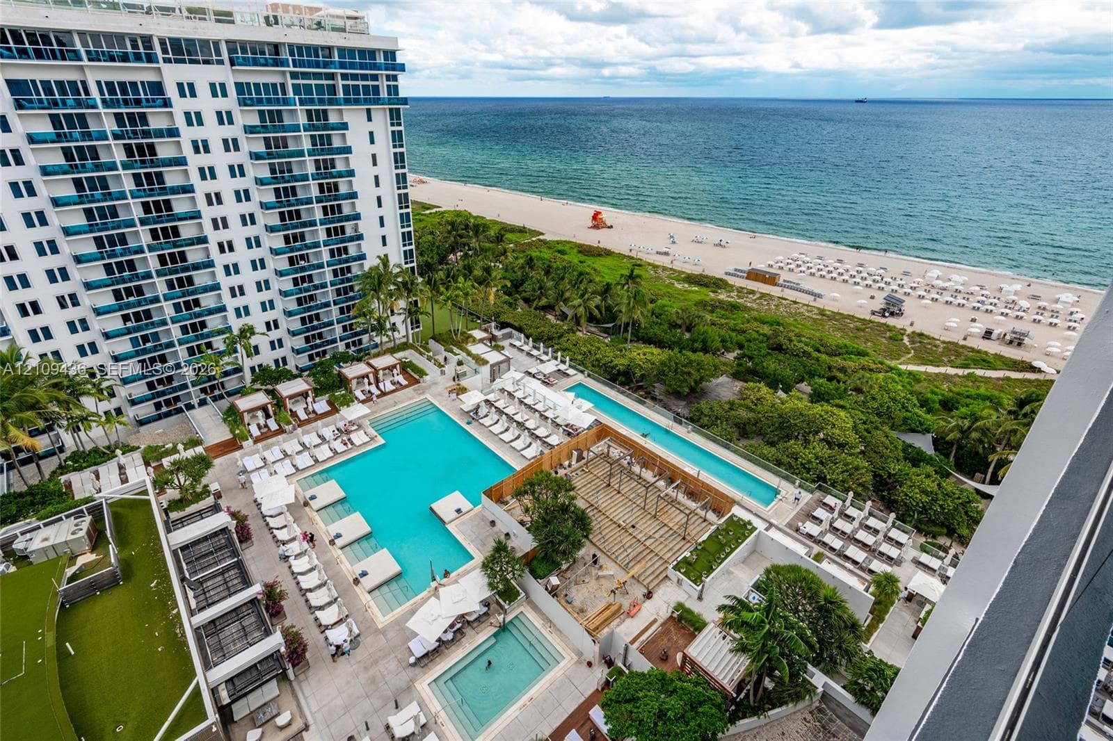 High-rise oceanfront property featuring multiple tiered swimming pools, extensive paved sun deck, structured pergola, and landscaped grounds