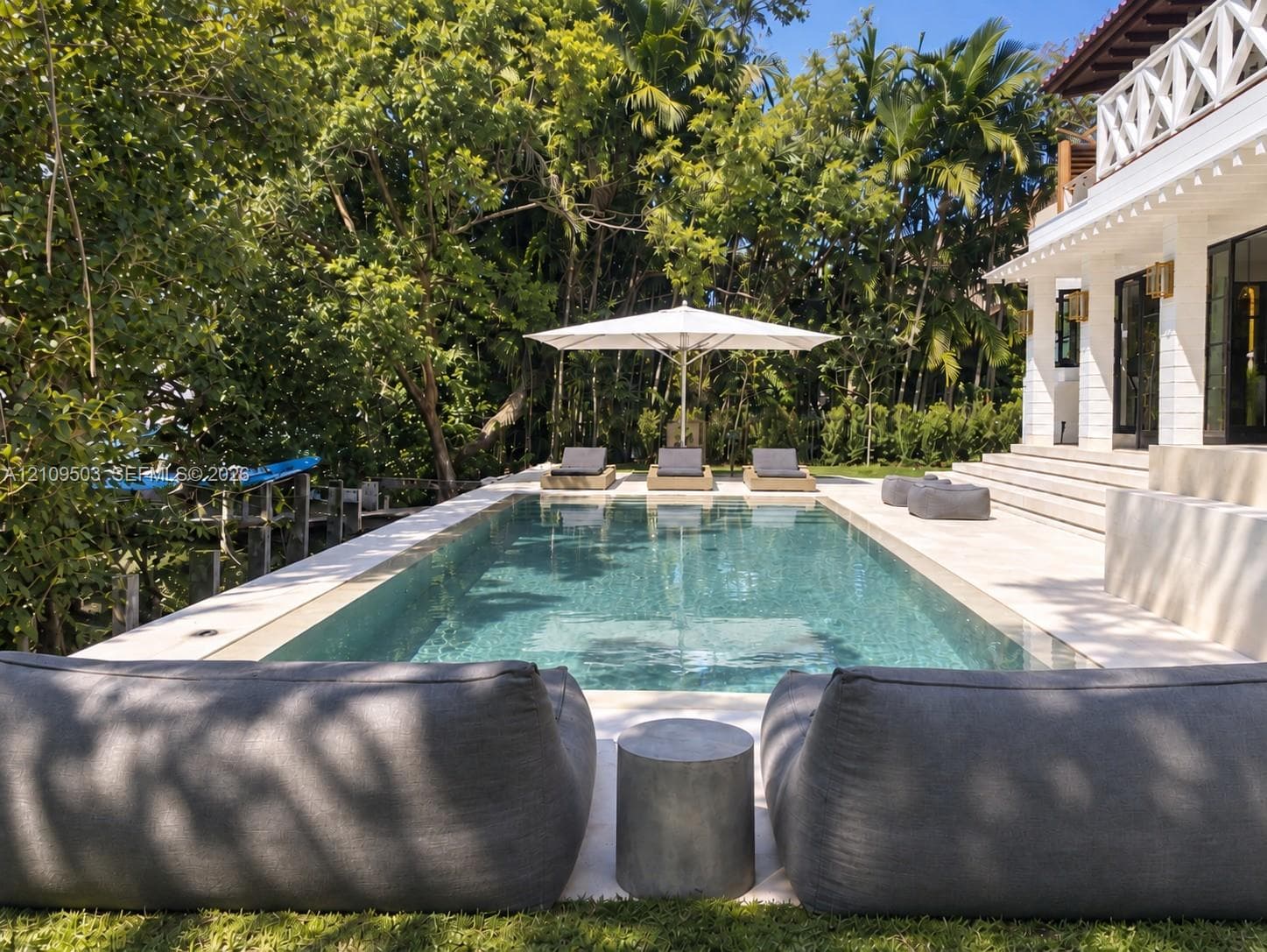 Rectangular swimming pool featuring stone coping, stone decking, tiered concrete stairs, and mature tropical landscaping