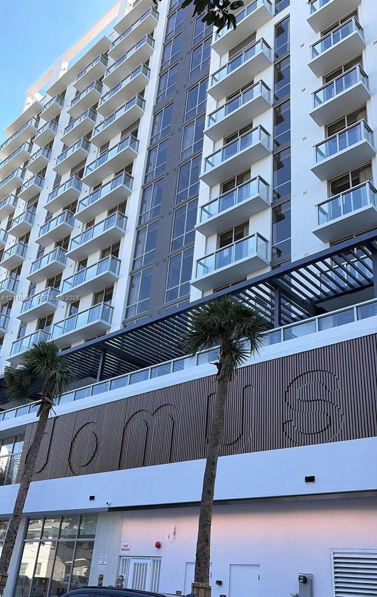 Multi-story modern building facade featuring glass balcony railings, vertical wood-slat accent paneling, and a structural metal pergola