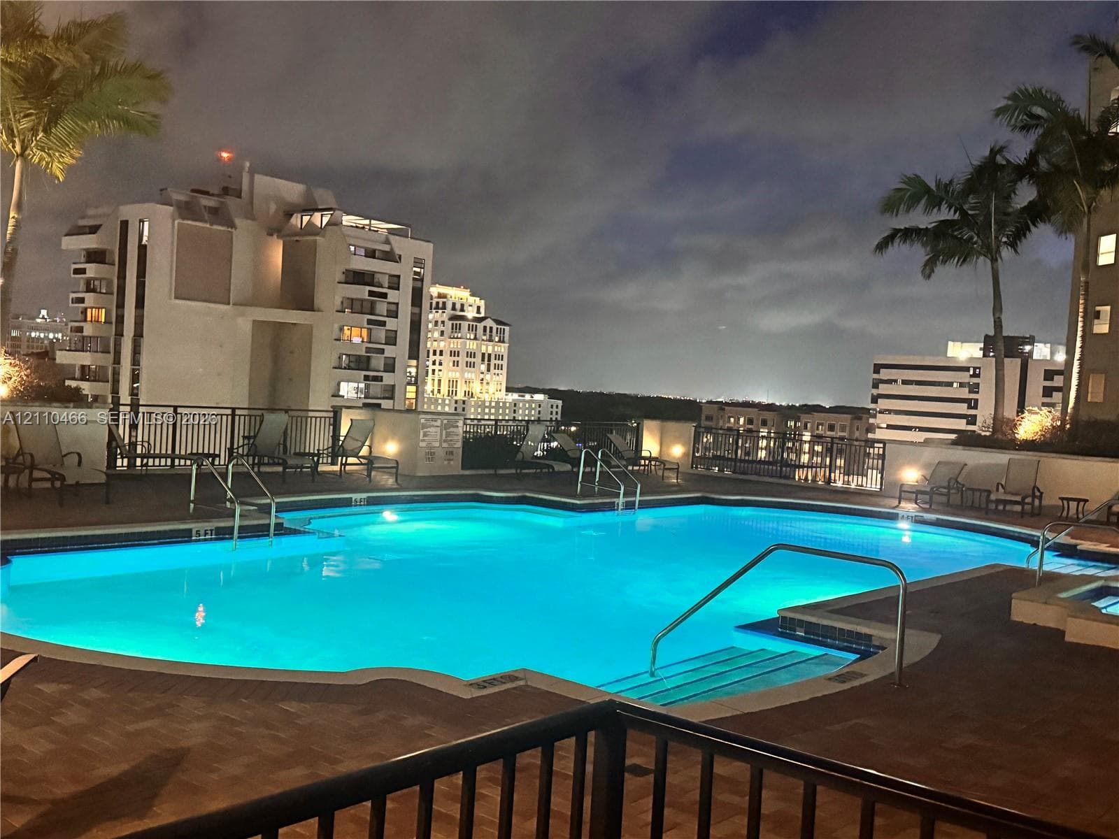 Swimming pool featuring a multi-level deck, integrated spa, perimeter metal fencing, and palm trees
